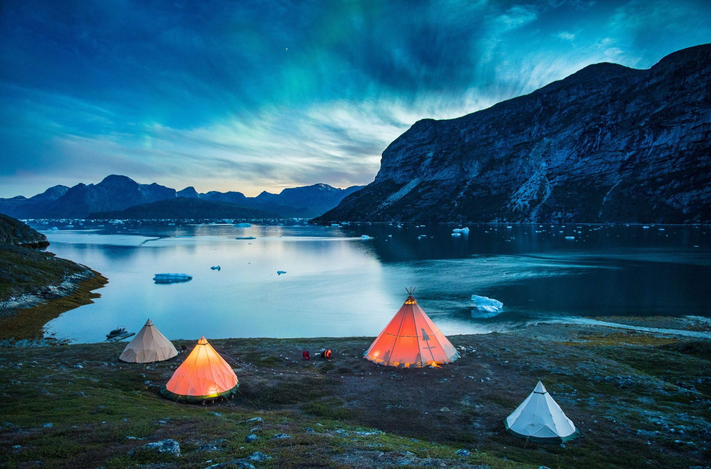 Lit tents beneath the aurora at Nomad Greenland